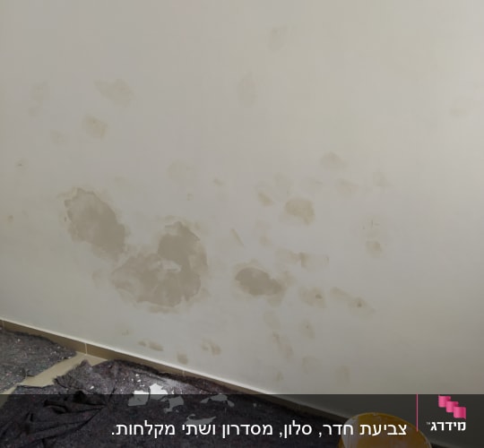 קיר עם תיקוני טיח, דלי צבע ומטלית על הרצפה